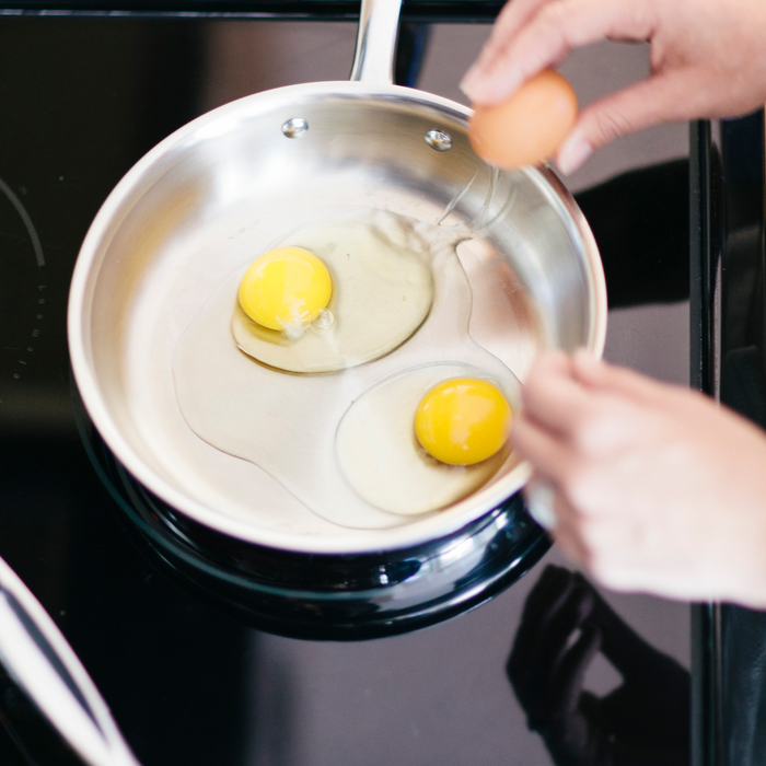 Close-up of 360 Cookware 7 Inch stainless steel fry pan with two raw eggs cooking on stovetop
