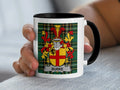 Black-accent Burke mug held in a hand, showing the red-and-gold shield on a tartan background.