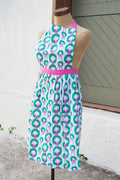 Mannequin wearing a holiday patterned apron with a pink belt against a white wall.