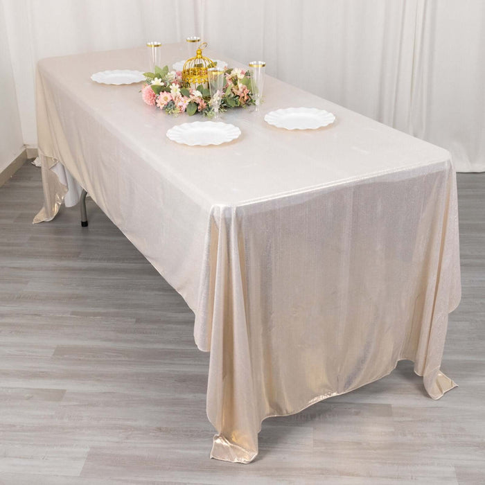 Elegant table setup with gold tablecloth, floral centerpiece, and white plates.