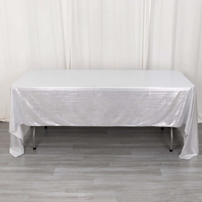 Shiny silver tablecloth draped over a white table in a studio setting.