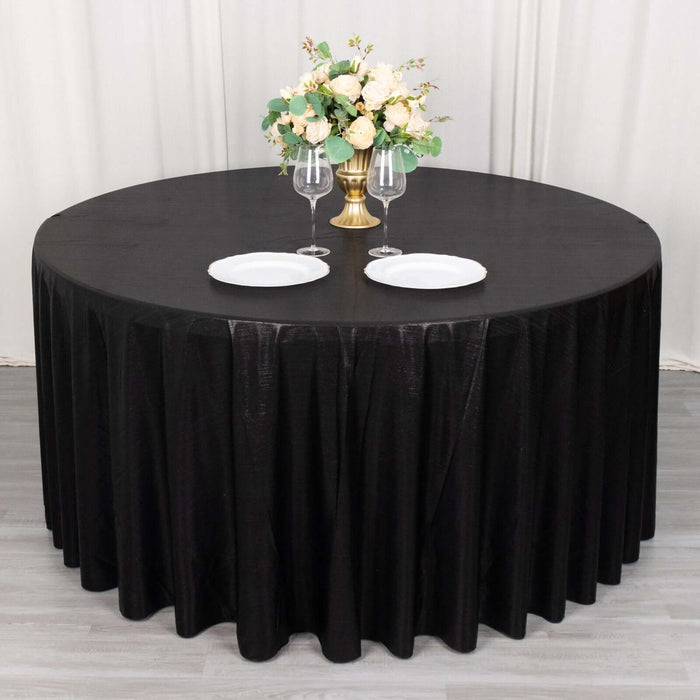 Black round table with elegant floral centerpiece and plates set for dining.