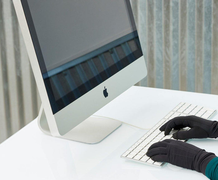Black thin warm Writer's Glove typing gloves worn on hands using white computer keyboard with iMac monitor