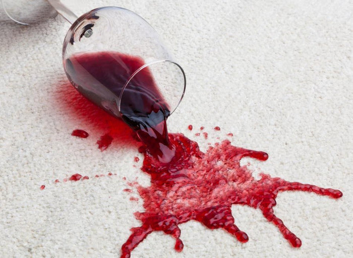 Close-up of red wine spilled from a tipped glass onto light-colored carpet creating a large stain